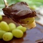 Spoonful of grape dessert, with vanilla cream underneath, grape in the middle and creamy chocolate on top