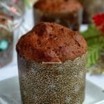 Mini chocotone dentro de forminha de papel tradicional sobre prato quadrado branco pequeno, ao fundo mais mini panetones desfocados