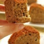 Mão segurando pedaço de bolo mordido, abaixo uma fatia de bolo sobre um prato quadrado pequeno