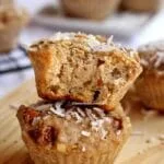 Bolinho de banana com cobertura de coco em flocos mordido sobre outro bolinho inteiro em uma tábua de madeira