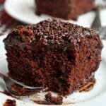 Fatia de bolo de chocolate com cobertura de chocolate que já foi comido alguns pedaços e o garfinho está ao lado da fatia