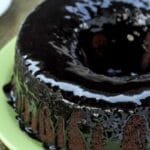 Bolo redondo com furo no meio de chocolate com cobertura de chocolate sobre prato verde claro
