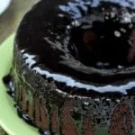 Bolo redondo com furo no meio de chocolate com cobertura de chocolate sobre prato verde claro