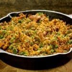 Caçarola de ferro fundido sobre tábua de madeira, dentro frango com arroz e ervilha