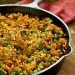 Caçarola de ferro fundido sobre tábua de madeira, dentro frango com arroz e ervilha mais temperos