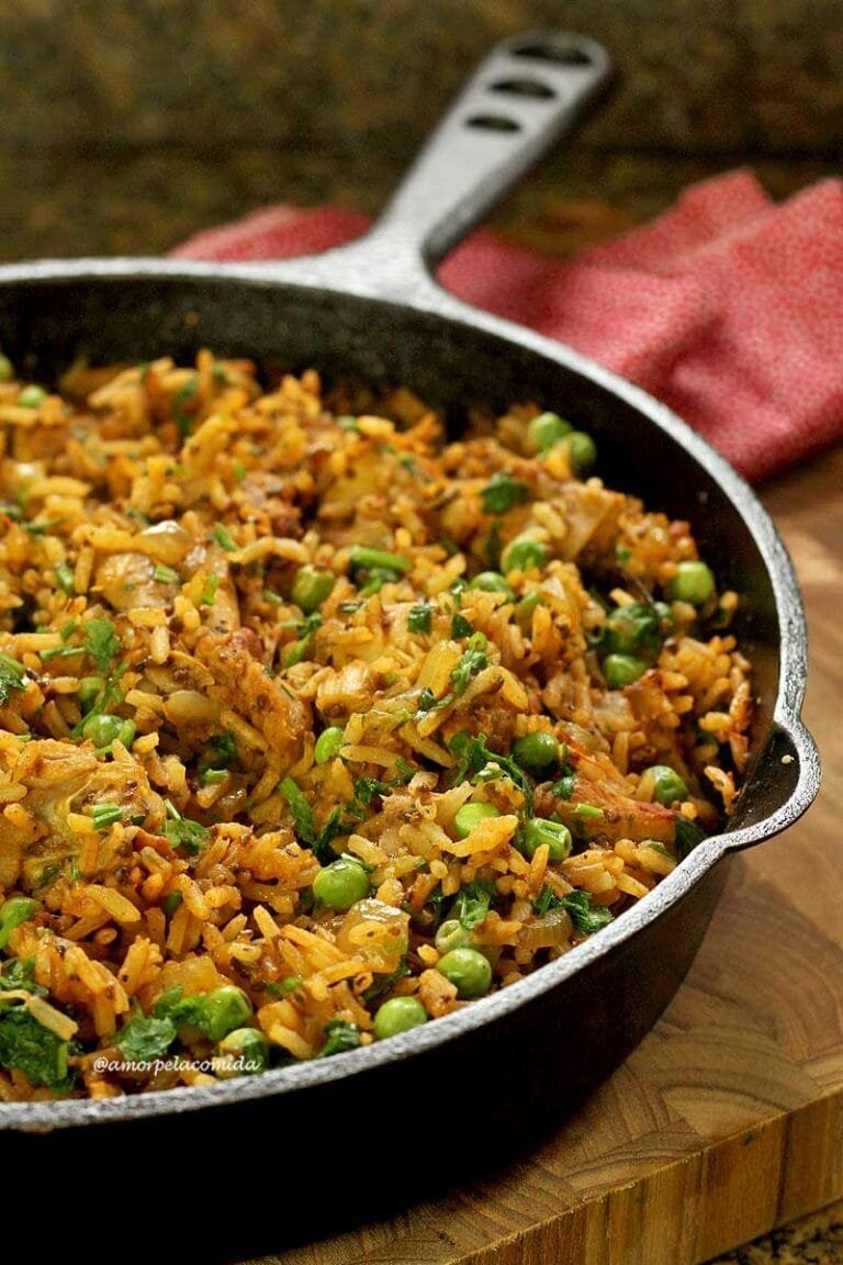 Cazuela de hierro fundido sobre una tabla de madera, dentro de pollo con arroz y guisantes más condimentos