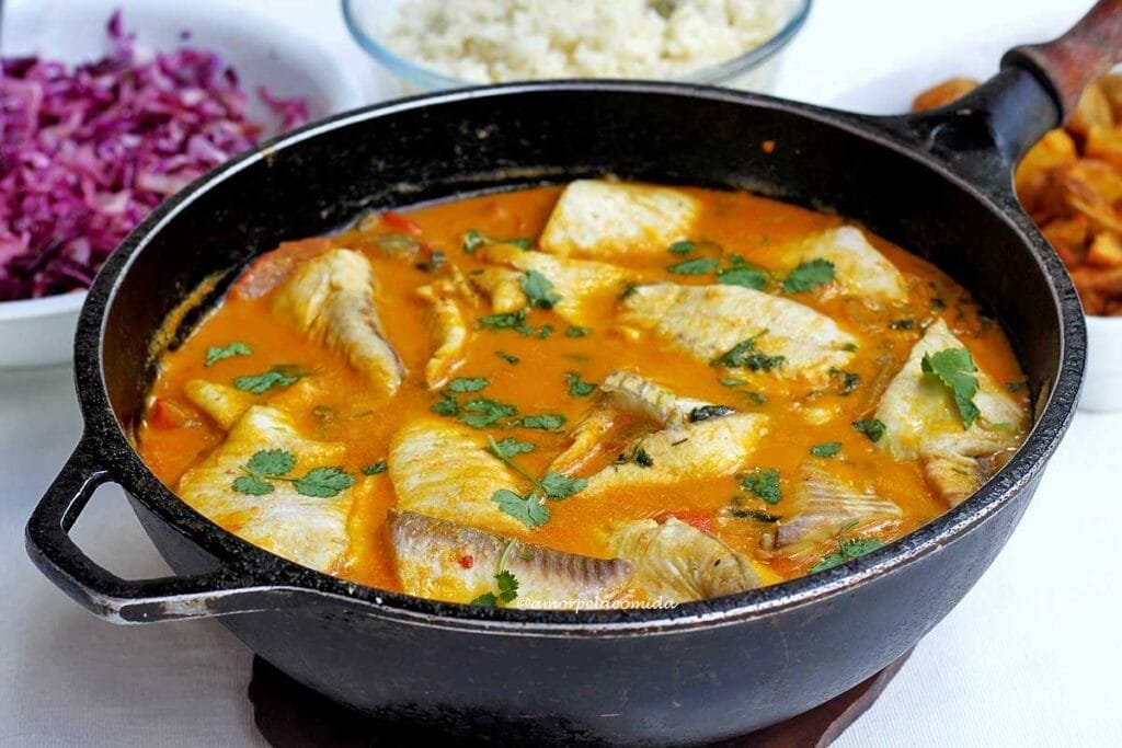 Panela preta grande com peixe ensopado em caldo a base de tomate, leite de coco e óleo de dendê