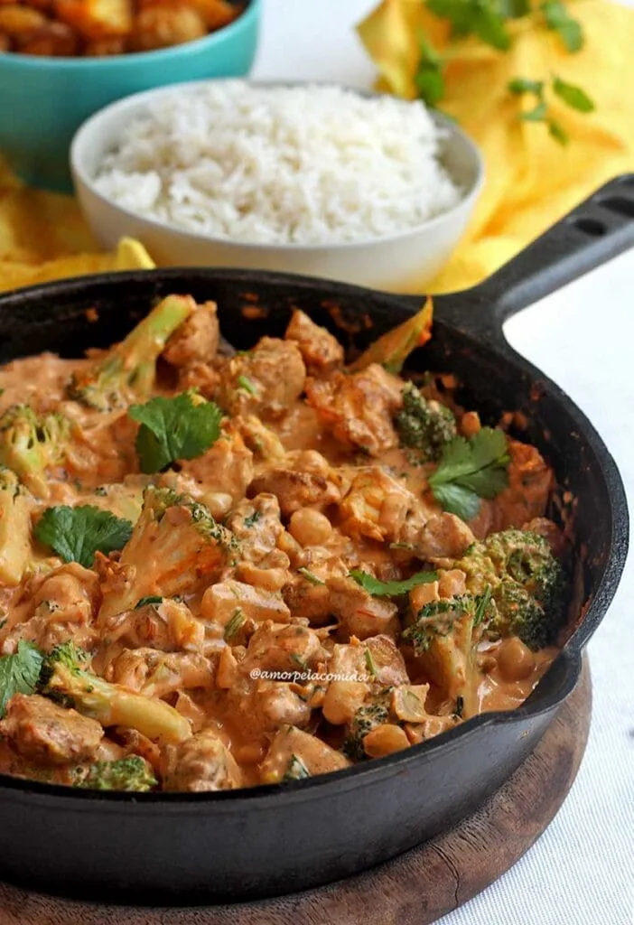 Black iron casserole with diced chicken in a creamy sauce with broccoli and chickpeas