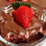 Pote de vidro redondo, canelado com sobremesa de morango dentro, por baixo bolo de chocolate, no meio creme com morango e por cima chocolate e um morango decorando