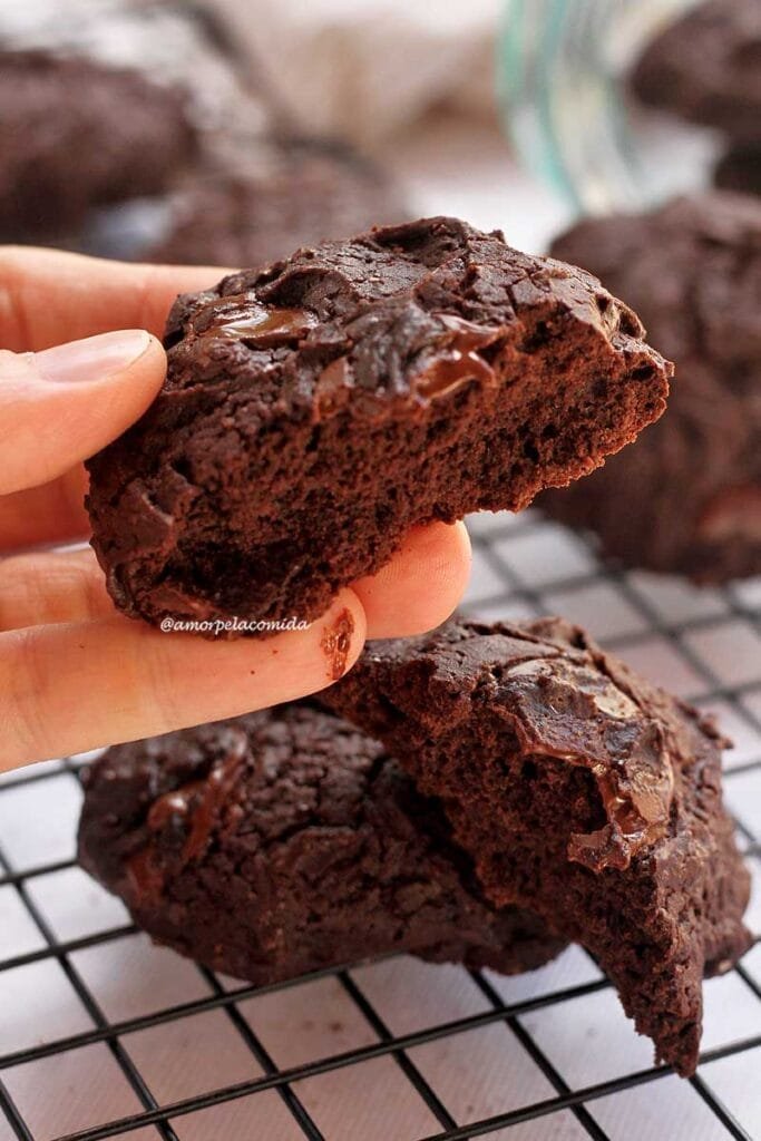 Mão segurando biscoito de chocolate partido ao meio mostrando a textura aerada do biscoito