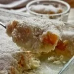 Serving spoon with peach dessert, cream and sponge cake on the base, on the glass dish where the dessert was made
